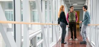 Three people standing in a glass hallway, chatting.