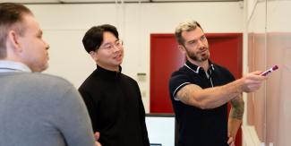 Three people standing while looking at a white board together.