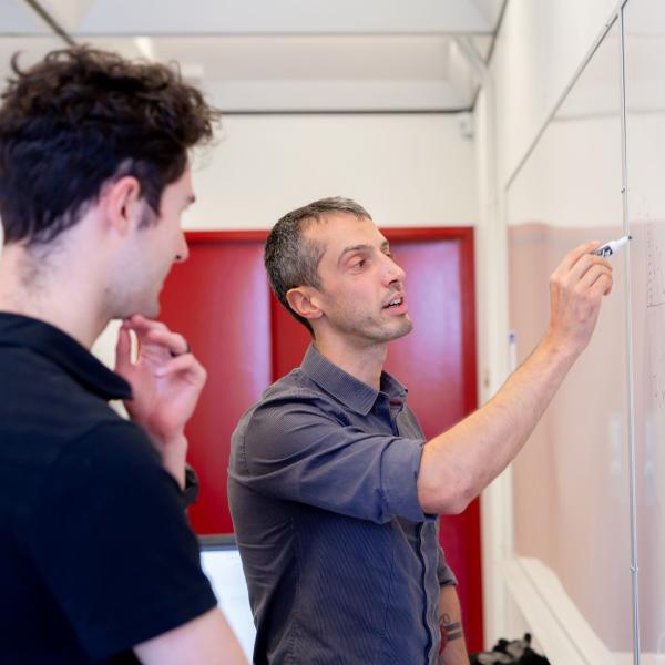 one person writing on the whiteboard explaining to another